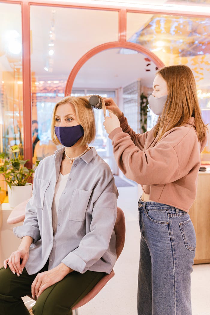 Woman receives hair styling in a salon with a stylist wearing face mask during new normal.